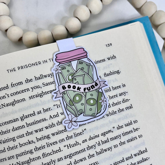 Magnetic bookmark with an illustration of a jar labeled 'Book Fund' filled with money, symbolizing saving for books